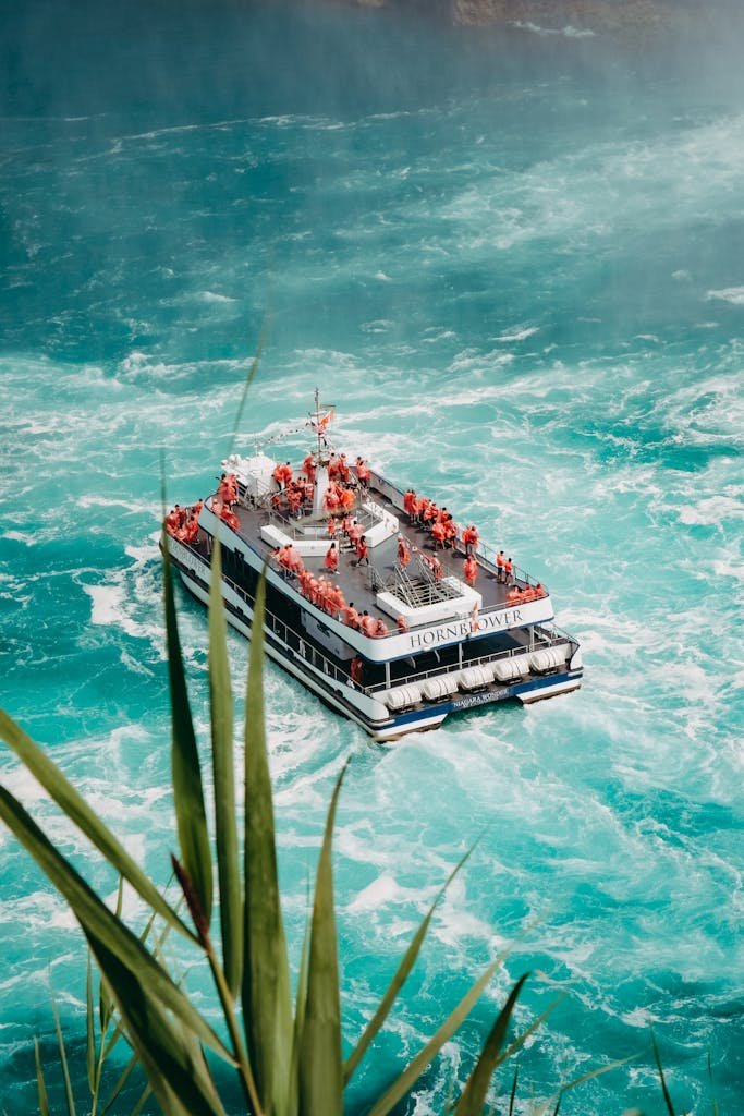 Tourists in orange jackets on a boat amidst powerful waters at Niagara Falls.